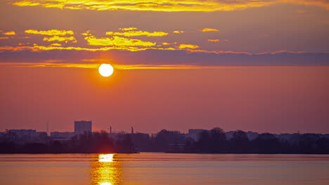 sun-rising-timelapse-over-coastal-city,-rays-reflecting-on-water-surface