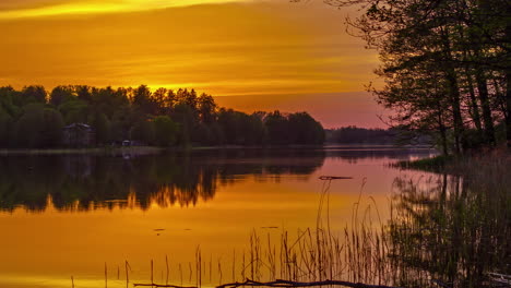 Golden-sky-sunset-over-water-timelapse,-with-trees-and-house-on-the-bank-of-the-lake-in-the-evening