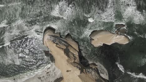 Vertical-aerial-view-of-sand-sea-cliffs-and-eroded-sea-stack-in-Peru