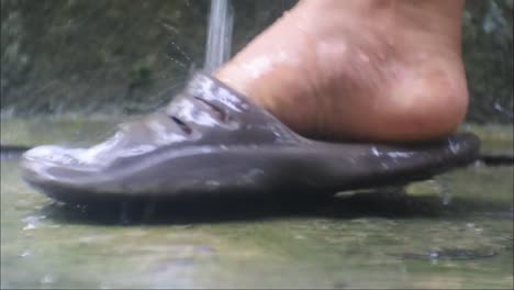close-up-of-feet-being-washed-with-water-from-the-faucet,-Water-flows-from-the-faucet-in-slow-motion,-washing-feet-in-sandals
