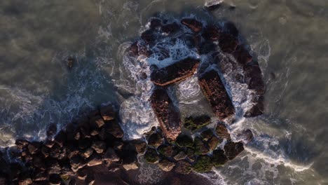 Top-down-aerial-shot-of-waves-crashing-on-a-man-made-rock-pool-with-a-slow-zoom-in-on-the-pool-as-the-waves-get-more-intense