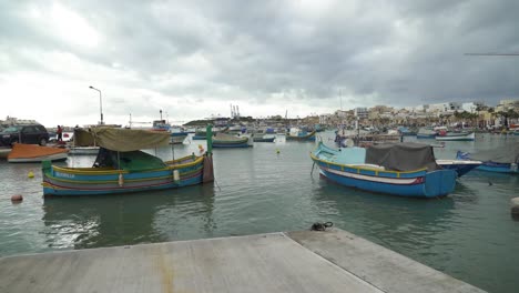 Mehrfarbige-Traditionelle-Maltesische-Fischerboote-Mit-Häusern-Im-Hintergrund-In-Marsaxlokk