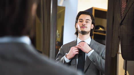 Young-bearded-man-trying-on-suit-in-front-of-fashion-boutique-mirror