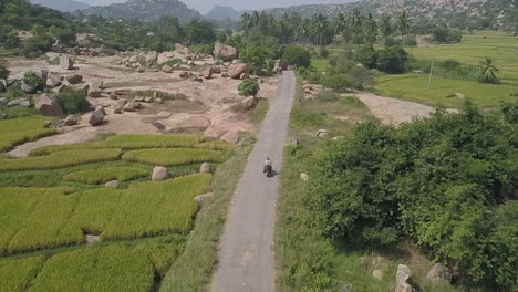 Aerial-follows-motorcycle-through-natural-wonder,-Hampi-valley,-India