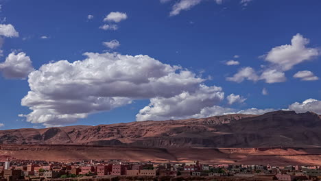 Time-lapse-shot-of-flying-white-clouds-on-blue-sky-over-red-mountains-and-small-african-city-in-desert-of-Morocco