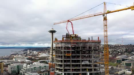 Aerial-of-a-crane-construction-site-creating-a-skyscraper-with-the-Seattle-Space-Needle-in-the-background