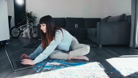 Young-woman-sitting-cross-legged-chatting-on-laptop-while-play-with-puzzle-in-modern-flat-house,-girl-sit-cross-legged-in-trendy-clothes-spend-leisure-time-wisely,-modern-smart-eco-friendly-apartment