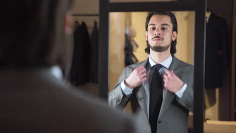 Zufriedener-Junger-Mann,-Der-Im-Modegeschäft-Einen-Anzug-Vor-Dem-Spiegel-Anprobiert