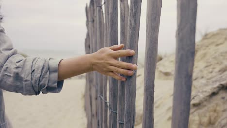 Young-woman-hand-touching-the-sitcks-of-a-wooden-wall-on-the-beach,-cloudy-beach