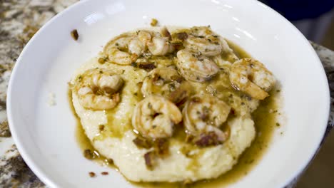 Sprinkling-chopped-bacon-on-a-plate-of-shrimp-and-grits