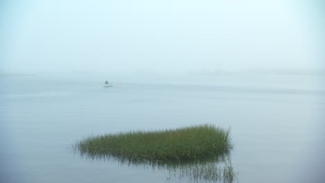 Wide-shot-of-man-rowing-a-row-boat-into-the-eerie-Maine-fog