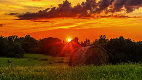 Time-lapse-shot-of-farmland-with-hay-bales-and-beautiful-orange-sunset-at-sky-in-backdrop---Flying-clouds-during-autumn-day-on-countryside-field