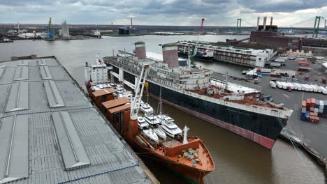 Old-decommissioned-ship-beside-new-freight-transport-with-many-boats