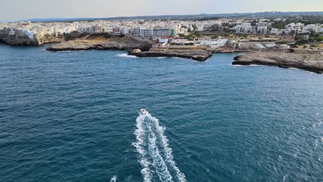 Aerial-drone-shot-of-a-motorboat-headed-to-Polignano-A-Mare,-Italy