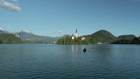 Couple-romantically-rowing-in-pletna-boat-towards-dreamy-Bled-island-on-lake,-aerial