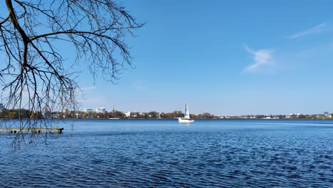 A-white-sailboat-slowly-moves-across-the-calm-Alster-lake-in-Hamburg-on-a-sunny-day