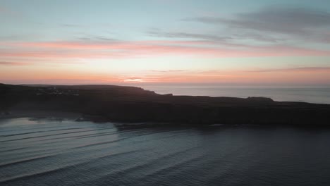 AERIAL:-Sideways-dolly-towards-coastal-cliffs-with-orange-sunrise-backdrop,-Rhossili-Gower,-4k-Drone