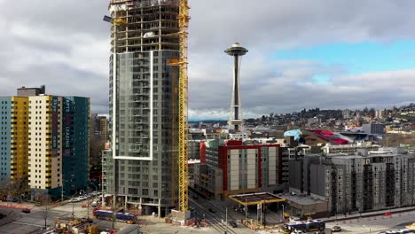 Descending-aerial-of-a-skyscraper-under-construction-with-the-Space-Needle-in-the-background
