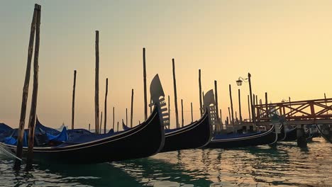 Low-angle-water-surface-pov-of-row-of-docked-gondolas-at-sunset,-Venice-in-Italy