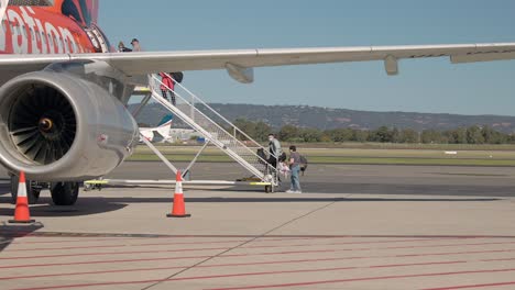Passengers-Boarding-Commercial-Air-Plane-Walking-Up-The-Ramp-Onto-The-Aircraft-From-Tarmac-Outside-On-A-Sunny-Day