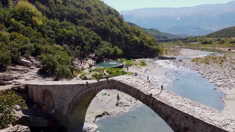 Stone-Arch-Bridge-and-People-Swim-in-Permet-Hot-Springs-and-Thermal-Baths,-Albania---Aerial,-Reveal