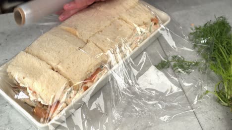 Close-up-meal-prep:-plastic-wrap-added-to-Smorgastarta-sandwich-cake