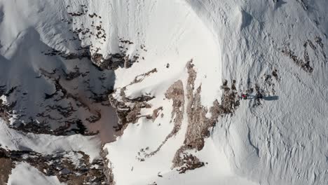 Top-down-drone-shot-of-hiker-walking-along-a-snowy-mountain-ridge-overlooking-a-steep-drop