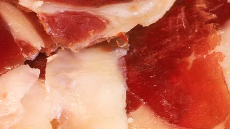 Slices-of-intense-spanish-serrano-ham-with-bread-rotating-on-wooden-board,-close-up-view-from-above
