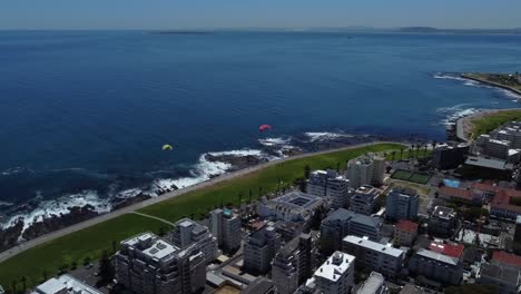 Drone-shot-of-Sea-Point,-Cape-Town---drone-is-flying-over-the-boulevard,-watching-the-ocean-and-some-paragliders