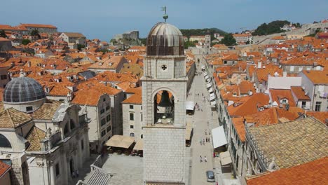 Dubrovnik,-Croatia:-Franciscan-Church-beside-Stradun-street-and-Monastery-in-Dubrovnik,-Croatia---old-town-in-summer,-at-noon-wit-tourists-strolling-along-the-road