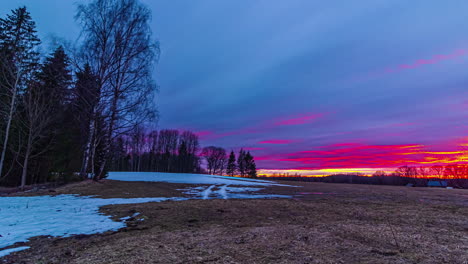 Rural-wooded-landscape-with-snow-melting,-sunset-time-lapse-with-flying-clouds