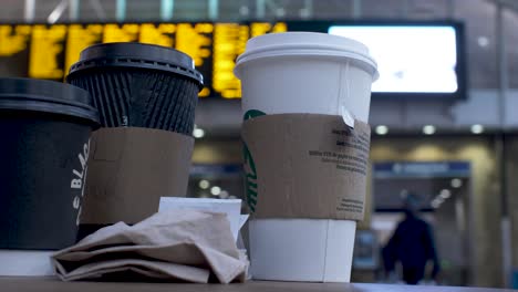 Group-Of-Disposal-Cups-On-Table-In-Kings-Cross-Train-Station-With-Bokeh-Background-Of-People-Going-Past