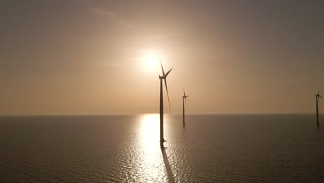 Dolly-shot-Wind-farm-on-calm-waters,-Silhouette-of-Windmills-spinning-during-sunset