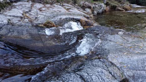 Water-stream-flowing-on-top-of-some-rocks-surface-creating-some-sort-of-rapids-and-waterfall