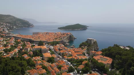 Toma-Aérea-De-Reenvío-De-Drones-De-Un-Casco-Antiguo-De-Dubrovnik,-Croacia-Con-Vistas-Al-Puerto-En-La-Costa-Y-Murallas-De-La-Fortaleza-Visibles-Desde-Arriba-En-Una-Noche-Nublada