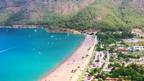 aerial-view-of-Adrasan-beach-on-a-hot-summer-day-in-Turkey-as-people-sun-bathe-while-boats-are-anchored-along-the-mountainous-Mediterranean-coastline