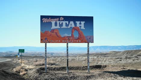 Leaving-Colorado-and-standing-in-front-of-the-Welcome-to-Utah-state-line-sign,-handheld