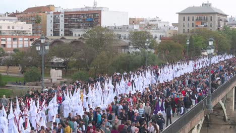 Penitentes-Marchan-Durante-Una-Procesión-Cruzando-El-Puente-De-Triana-En-Celebración-De-La-Semana-Santa-En-Sevilla,-España