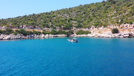 Aerial-drone-flying-towards-a-sailboat-anchored-in-the-tropical-blue-Mediterranean-Sea-alongside-a-rocky-beach-near-Finike-Turkey