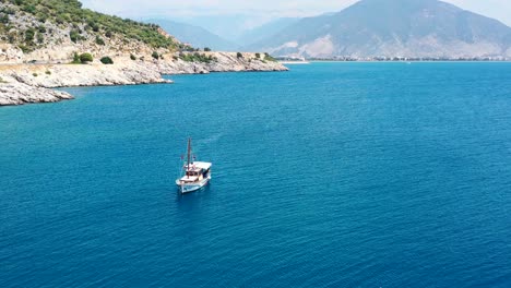 Aerial-drone-circling-a-turkish-sailboat-in-the-coastal-waters-of-the-Mediterranean-Sea-near-Finike-Turkey-on-a-sunny-summer-day-with-tropical-blue-water-and-large-mountains-in-the-distance