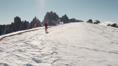 Wide-circling-drone-shot-of-trekker-walking-along-snowy-ridge-with-Candini-mountains-in-the-background