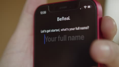 BeReal-logo-app-icon-on-mobile-phone-screen,-finger-tapping-on-display-to-start-application