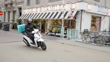 Deliveroo-delivery-boy-driving-a-scooter-in-the-historical-city-center-of-Ghent,-Belgium---Slow-motion