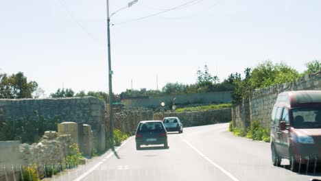 Driving-on-left-side-of-road-after-other-vehicles-in-Malta,-POV-view