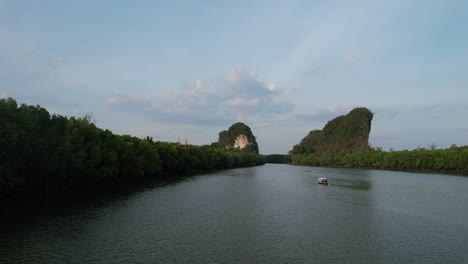 Aerial-drone-flying-low-along-a-river-and-mangrove-forest-approaching-a-thai-longtail-boat-and-limestone-mountain-rocks-in-the-distance-at-Krabi-Town-Thailand