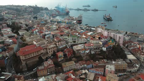 Aerial-orbit-of-Cerro-Concepcion-colorful-houses-and-Lutheran-Church,-Valparaiso-city-and-Sea-Port-in-the-back,-Chile