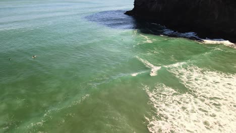 Aerial-video-of-Surfer-riding-right-hand-break-at-Piha-black-sand-beach-in-New-Zealand