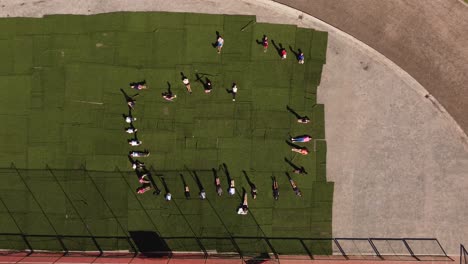 A-dynamic-descending-aerial-footage-of-a-group-of-students-lying-on-the-grass-of-the-athletic-stadium-while-doing-leg-raise-exercises