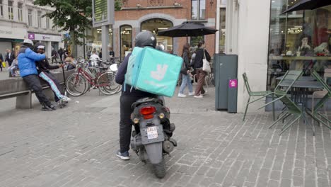 Weibliche-Deliveroo-Fahrerin-Auf-Einem-Roller,-Die-Vor-Dem-Stadtrestaurant-Auf-Essensbestellungen-Wartet-–-Gent,-Belgien