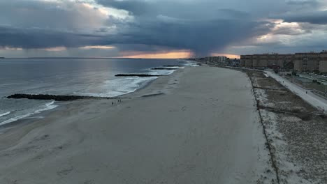 An-aerial-view-of-a-quiet-beach-in-Arverne,-NY-as-rain-falls-in-the-distance-on-a-cloudy-evening
